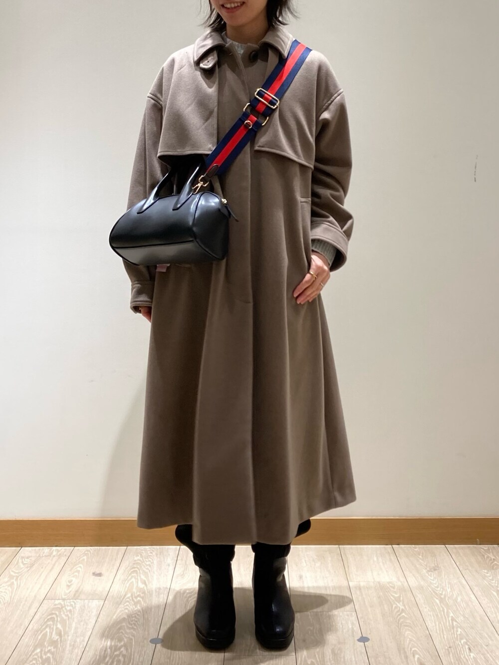 ブラウン系のステンカラーコート、ブラック系のボストンバッグ、ブラック系のブーツを着用したレディースの冬コーディネートの2枚目の写真