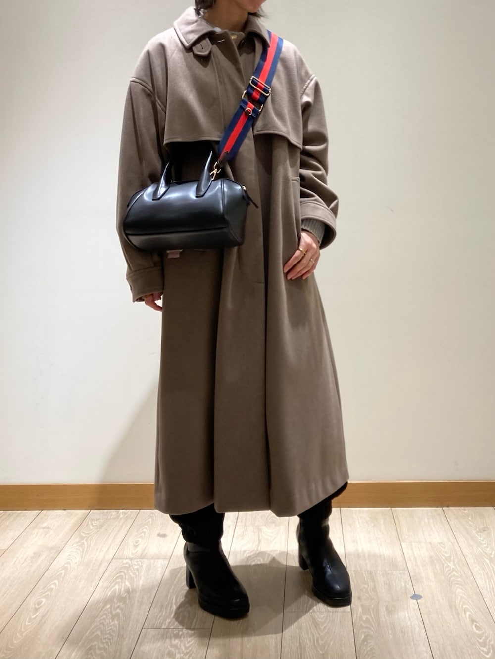 ブラウン系のステンカラーコート、ブラック系のボストンバッグ、ブラック系のブーツを着用したレディースの冬コーディネートの3枚目の写真