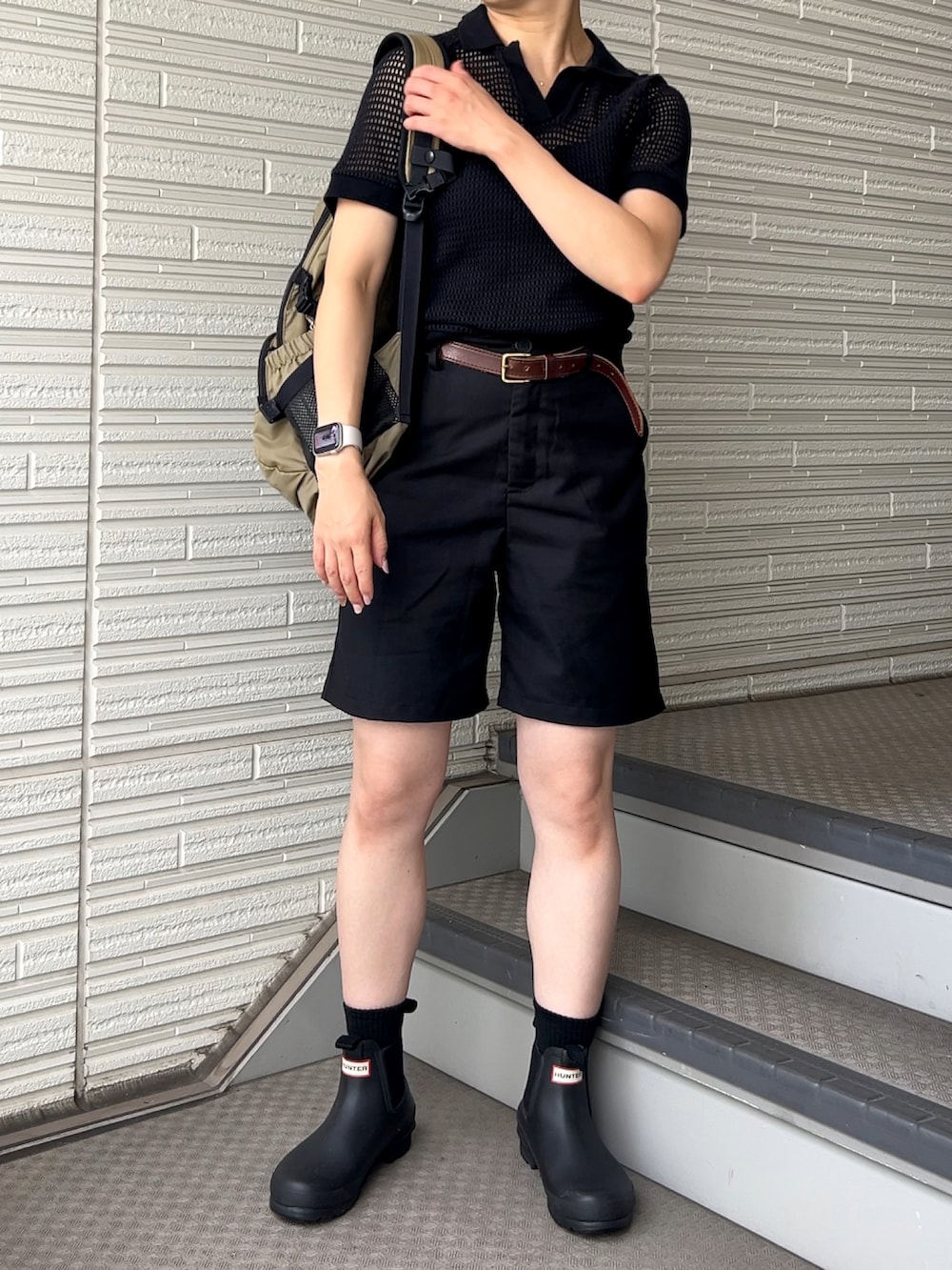 ブラック系のパンツ、ブラック系のポロシャツ、ベージュ系のバックパック/リュックを着用したレディースの夏コーディネートの2枚目の写真