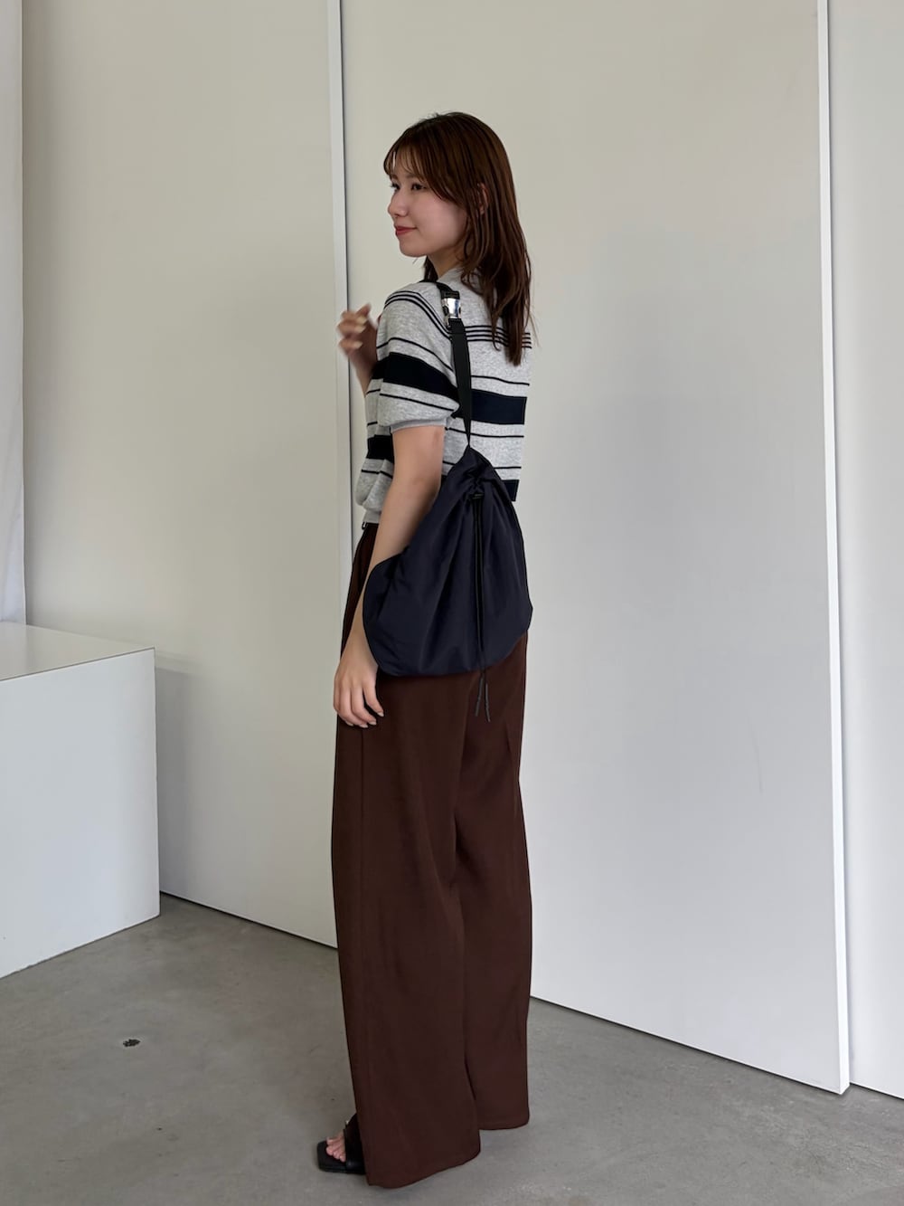 グレー系のニット/セーター、ブラウン系のスラックス、ブラック系のサンダルを着用したレディースの春コーディネートの2枚目の写真