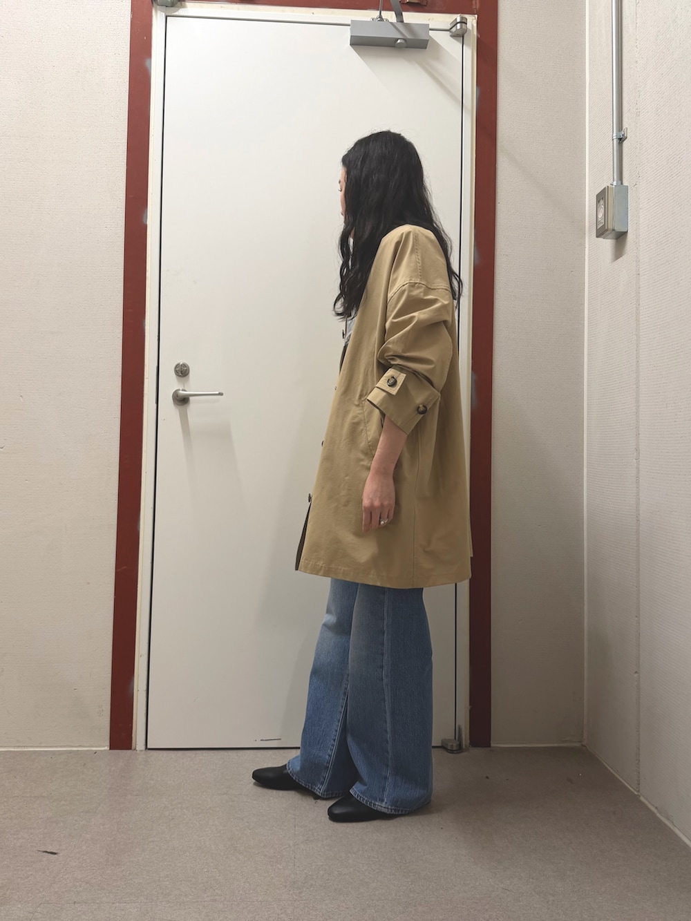 ベージュ系のステンカラーコート、ブルー系のデニムパンツ、ブラック系のその他シューズを着用したレディースの春コーディネートの2枚目の写真