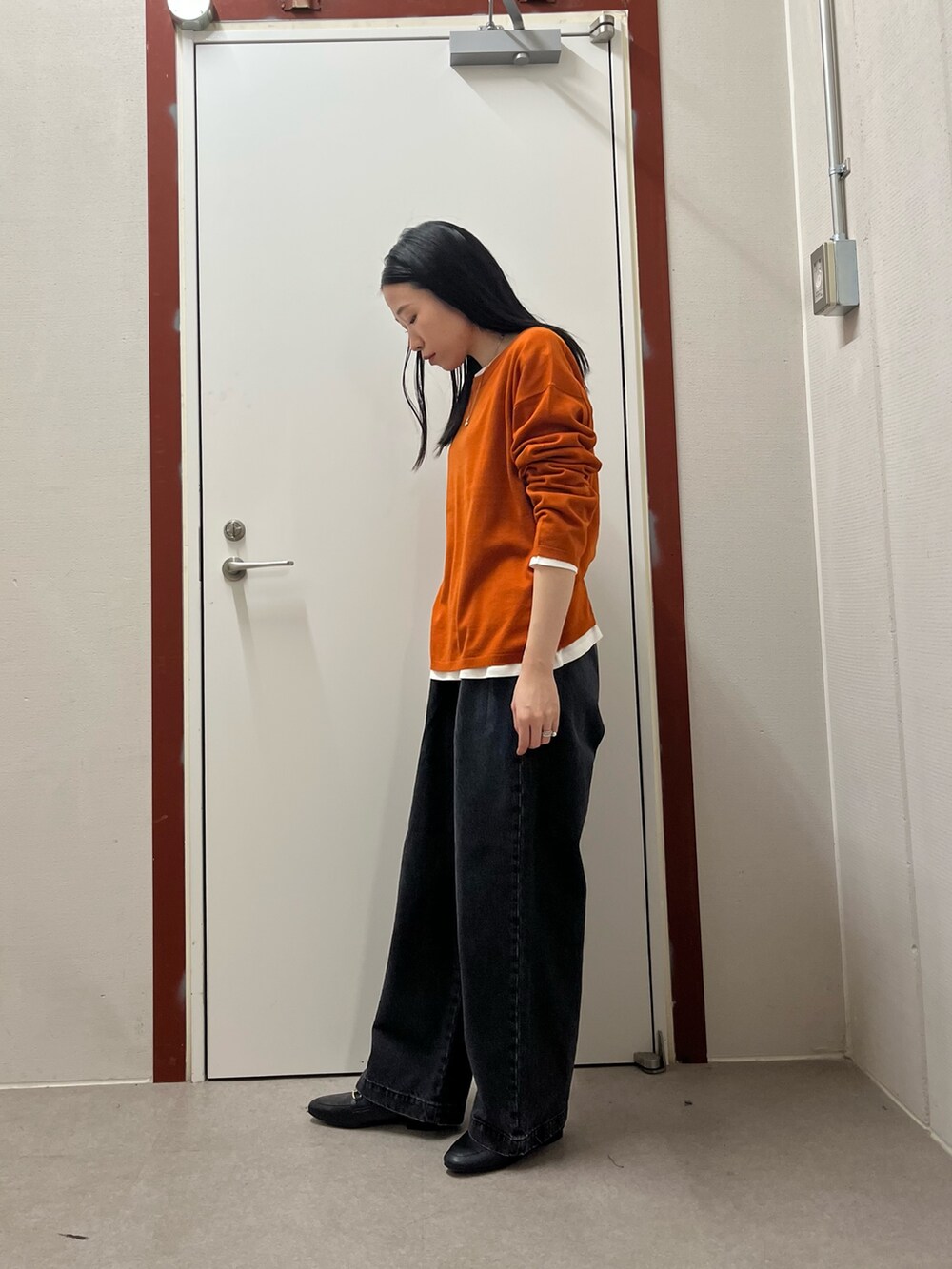 オレンジ系のニット/セーター、ブラック系のデニムパンツを着用したレディースの秋コーディネートの2枚目の写真