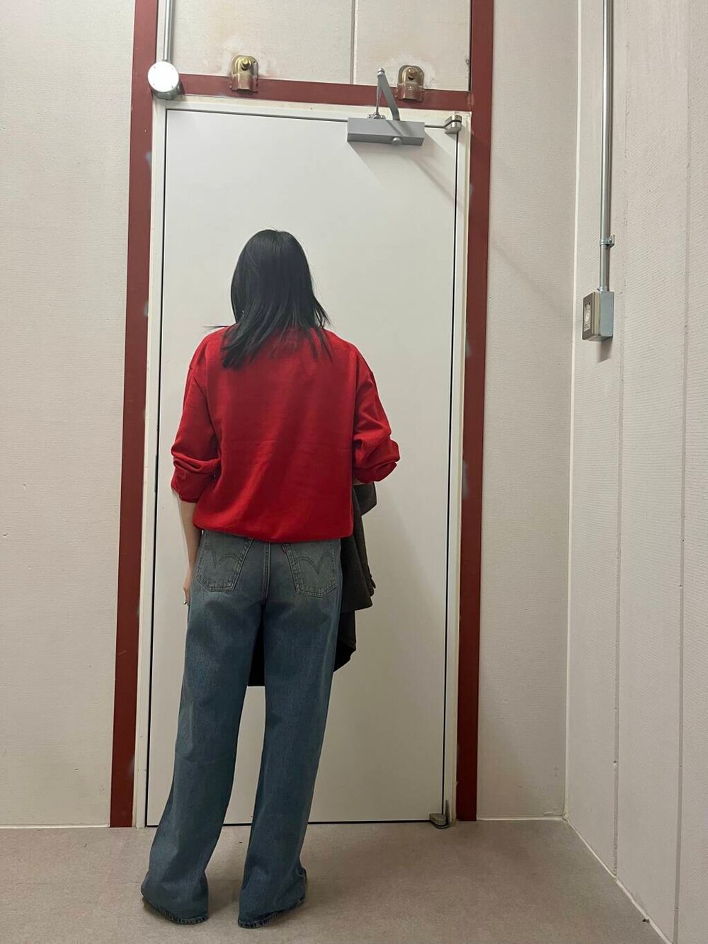 レッド系のニット/セーター、ブラック系のその他アウター、ブルー系のデニムパンツを着用したレディースの冬コーディネートの4枚目の写真