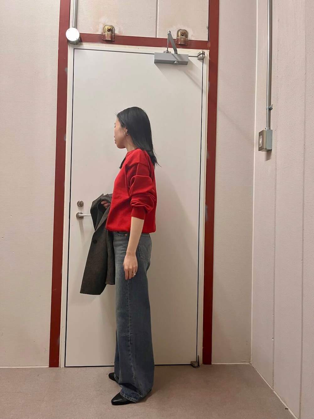 レッド系のニット/セーター、ブラック系のその他アウター、ブルー系のデニムパンツを着用したレディースの冬コーディネートの3枚目の写真