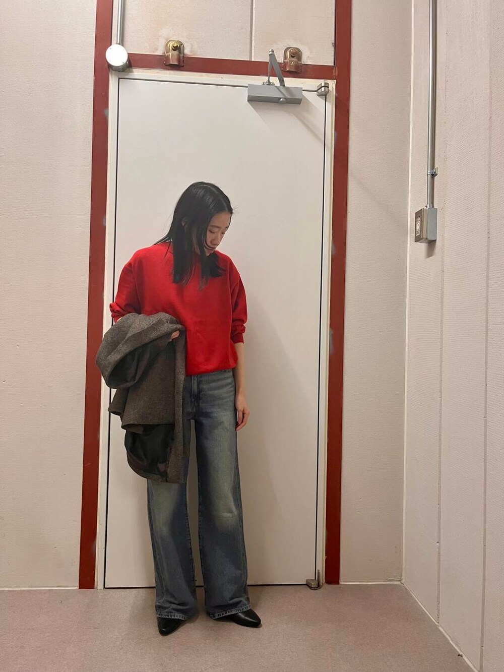 レッド系のニット/セーター、ブラック系のその他アウター、ブルー系のデニムパンツを着用したレディースの冬コーディネートの2枚目の写真