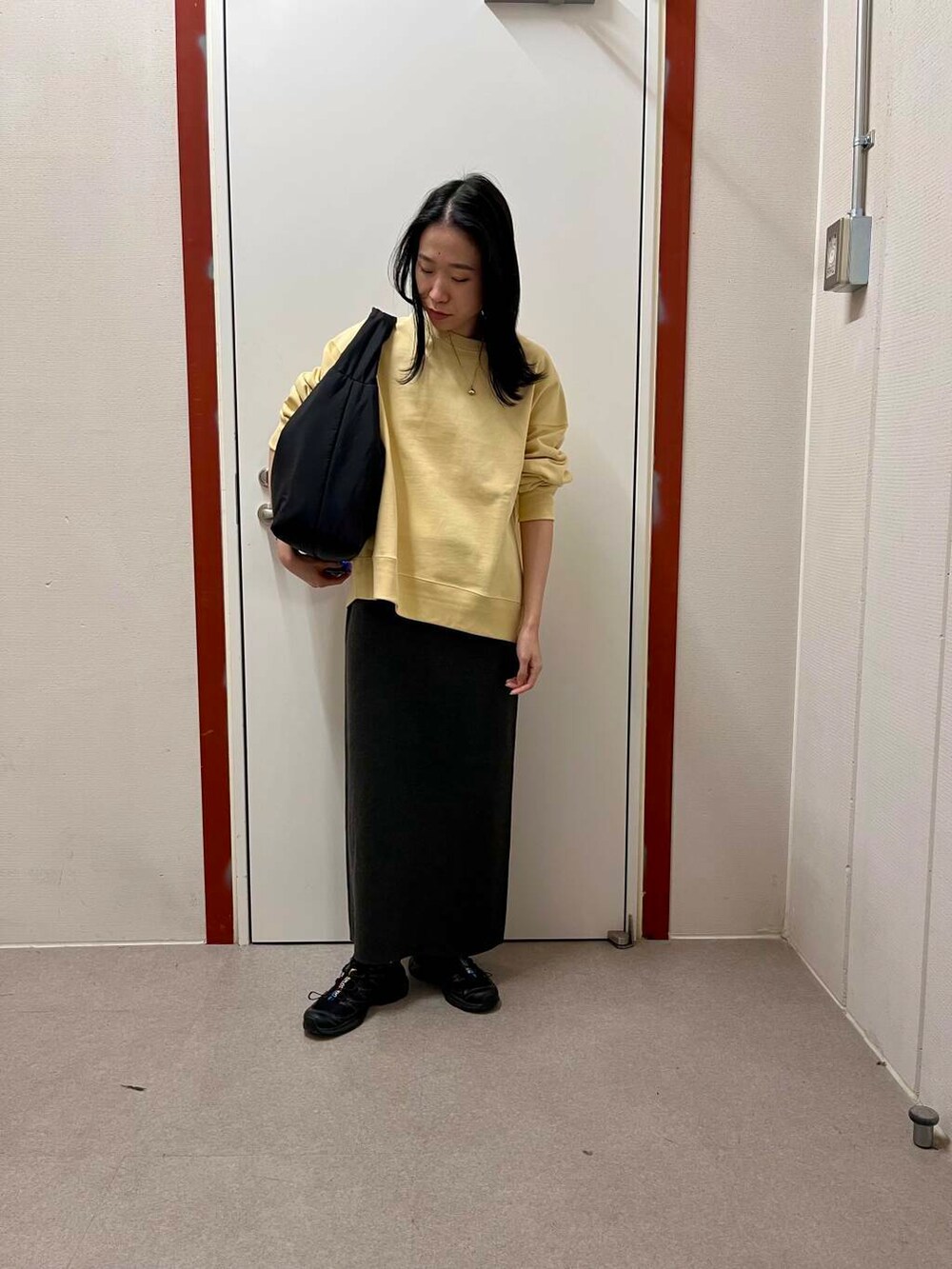 グレー系のスカート、ブラック系のトートバッグ、イエロー系のスウェットを着用したレディースの冬コーディネートの2枚目の写真