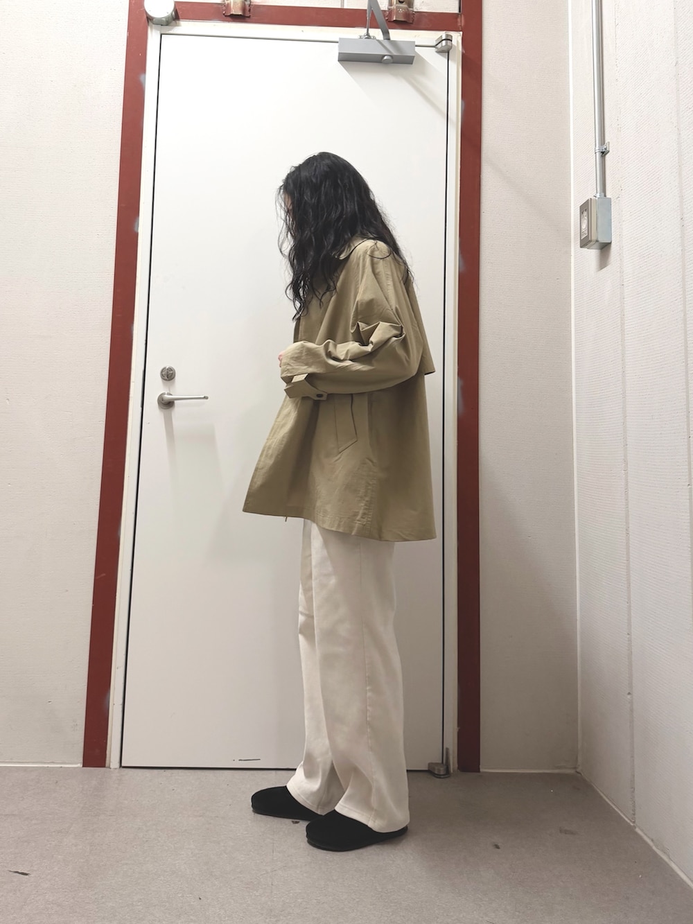 ベージュ系のステンカラーコート、ホワイト系のその他パンツ、ブラック系のサンダルを着用したレディースの冬コーディネートの2枚目の写真