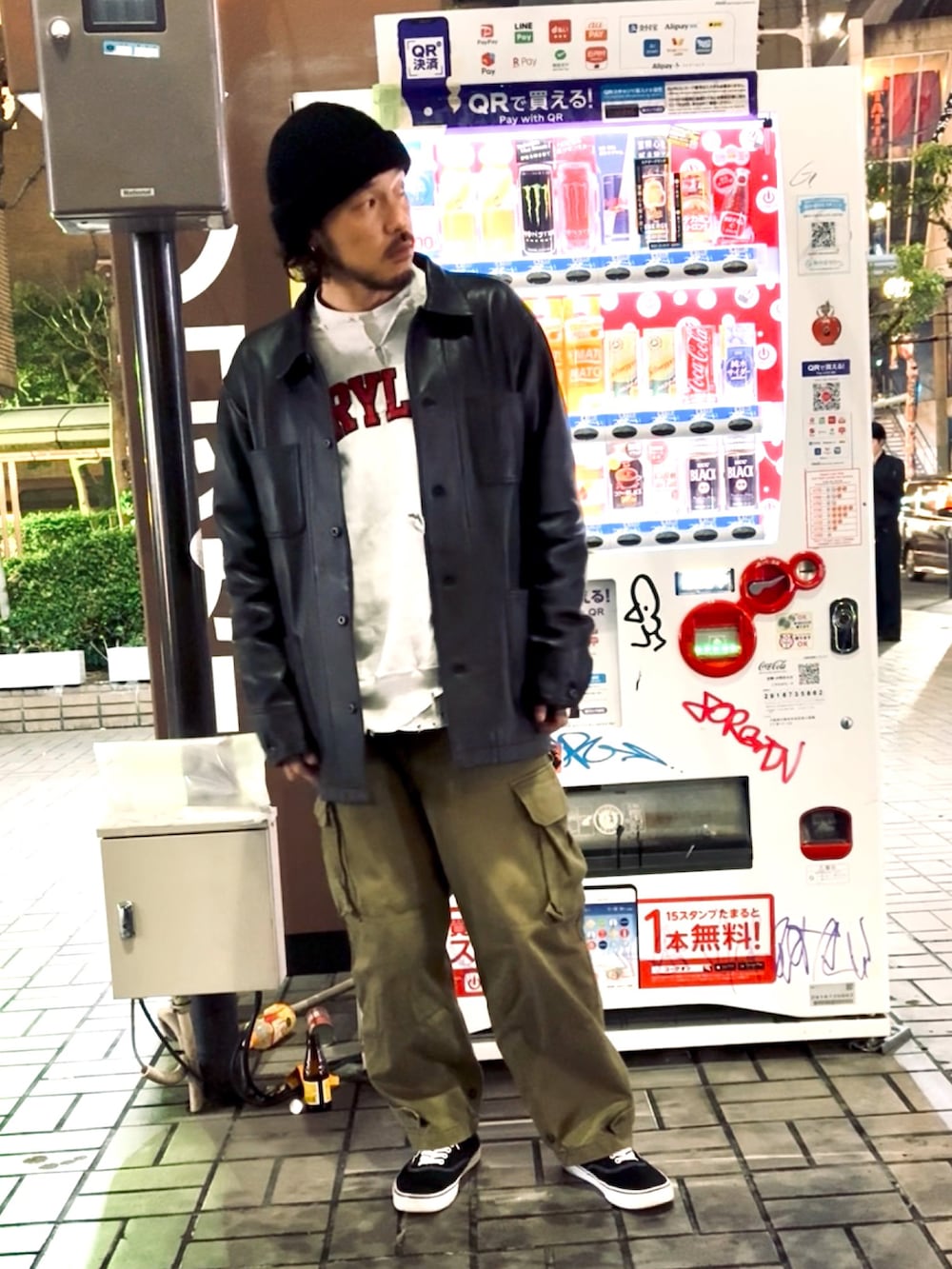 グリーン系のカーゴパンツ、ブラック系のスニーカー、ブラック系のライダースジャケットを着用したメンズの春コーディネートの2枚目の写真