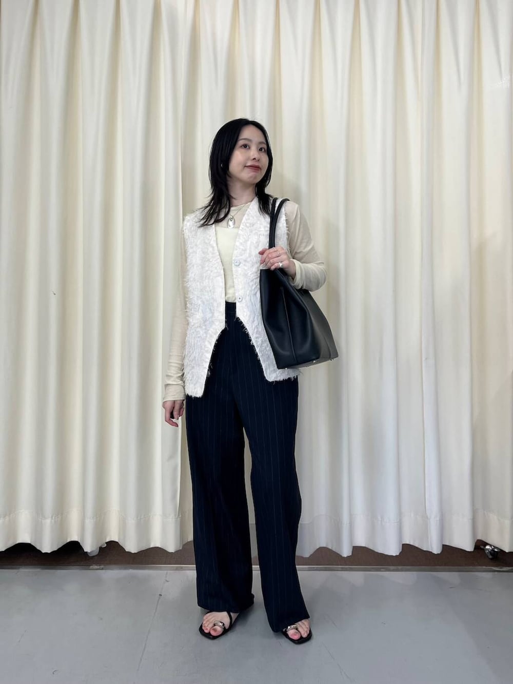 ホワイト系のベスト、ブラック系のサンダル、ブラック系のショルダーバッグを着用したレディースの春コーディネートの3枚目の写真