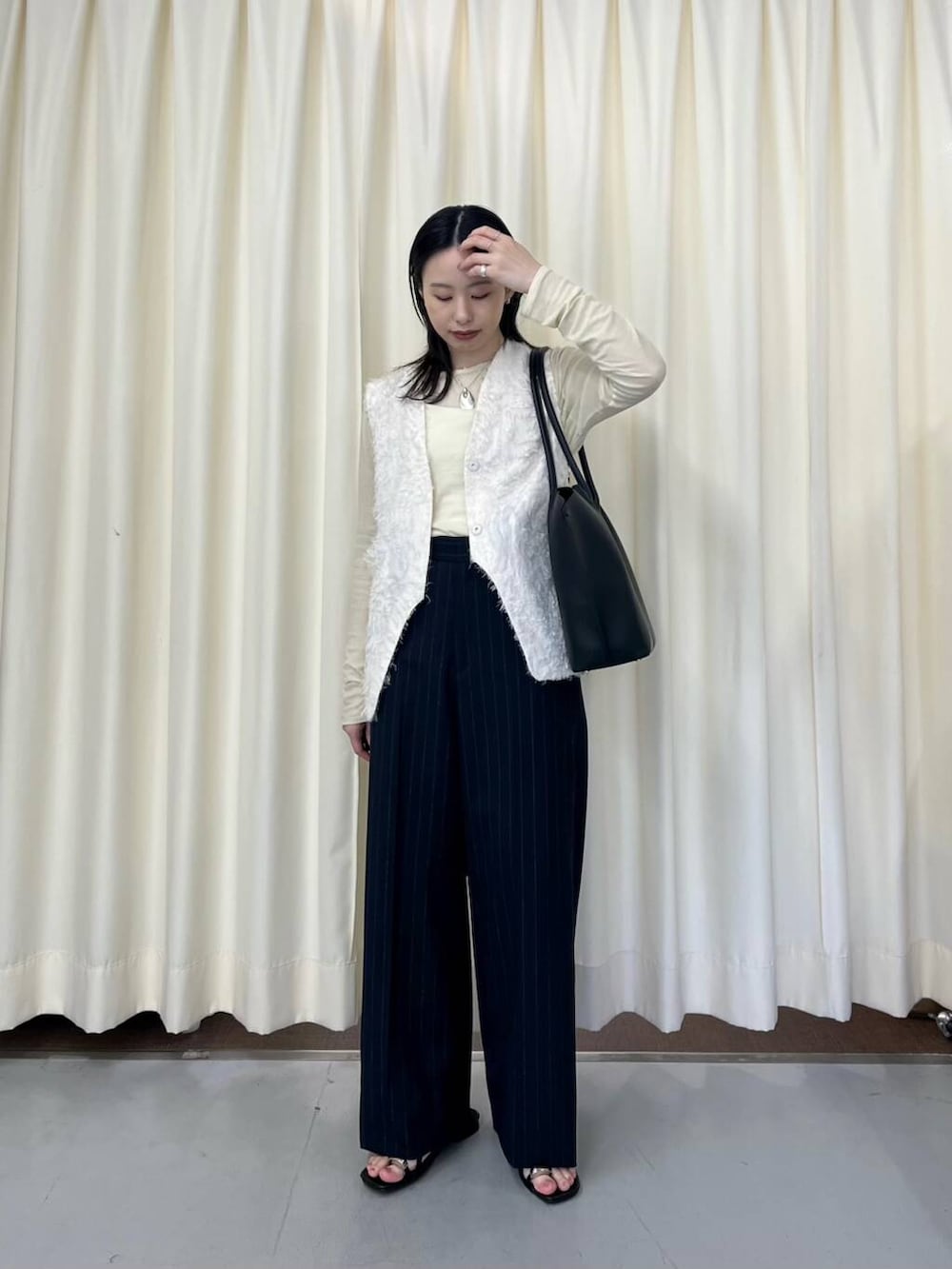 ホワイト系のベスト、ブラック系のサンダル、ブラック系のショルダーバッグを着用したレディースの春コーディネートの2枚目の写真