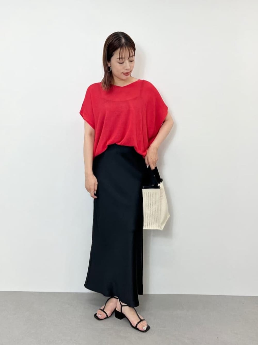 ピンク系のニット/セーター、ブラック系のスカート、ホワイト系のハンドバッグを着用したレディースの夏コーディネートの3枚目の写真