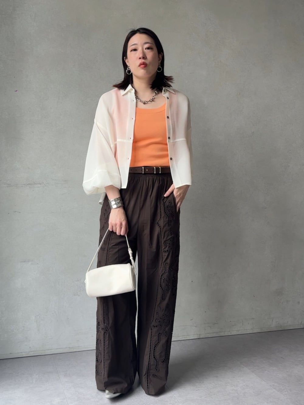 ブラウン系のその他パンツ、ホワイト系のシャツ/ブラウス、オレンジ系のニット/セーターを着用したレディースの春コーディネートの2枚目の写真