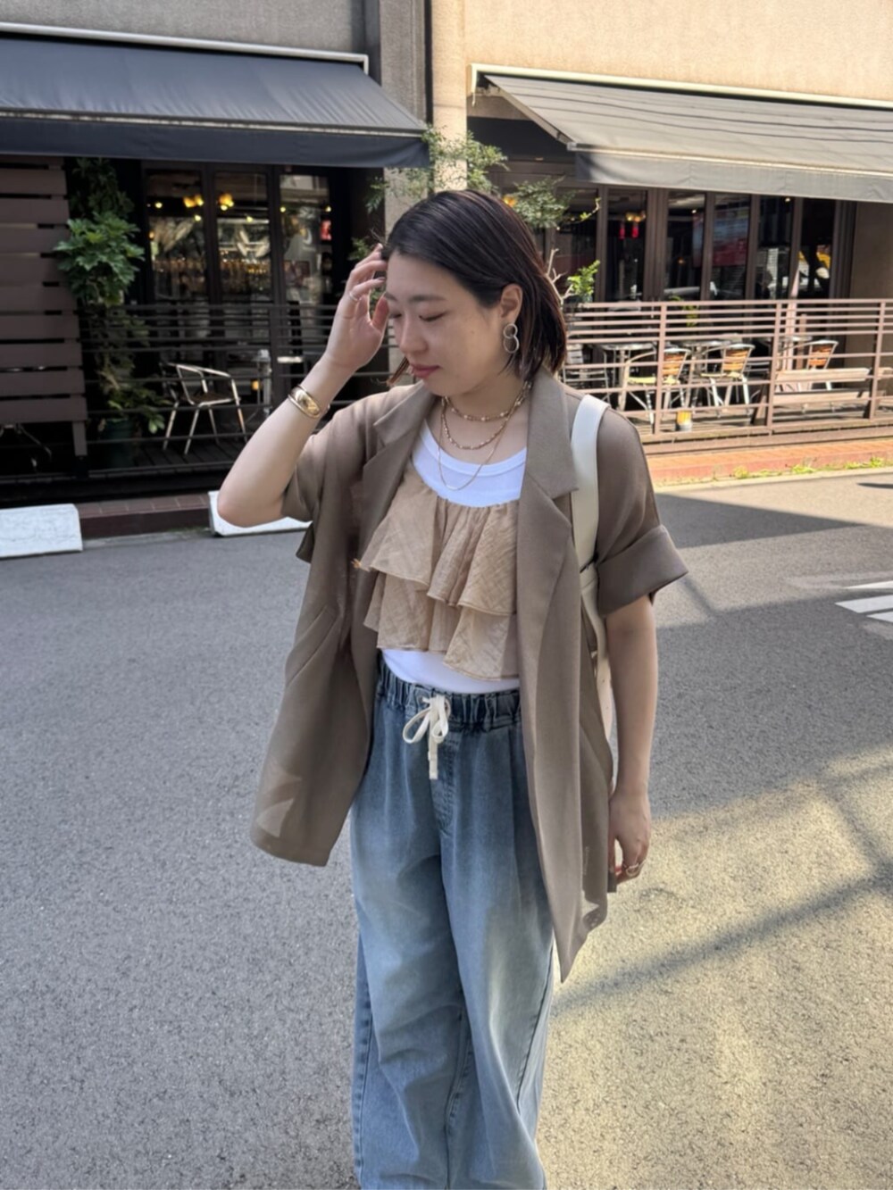 ホワイト系のショルダーバッグ、ブルー系のデニムパンツ、ブラウン系のテーラードジャケットを着用したレディースの春コーディネートの9枚目の写真