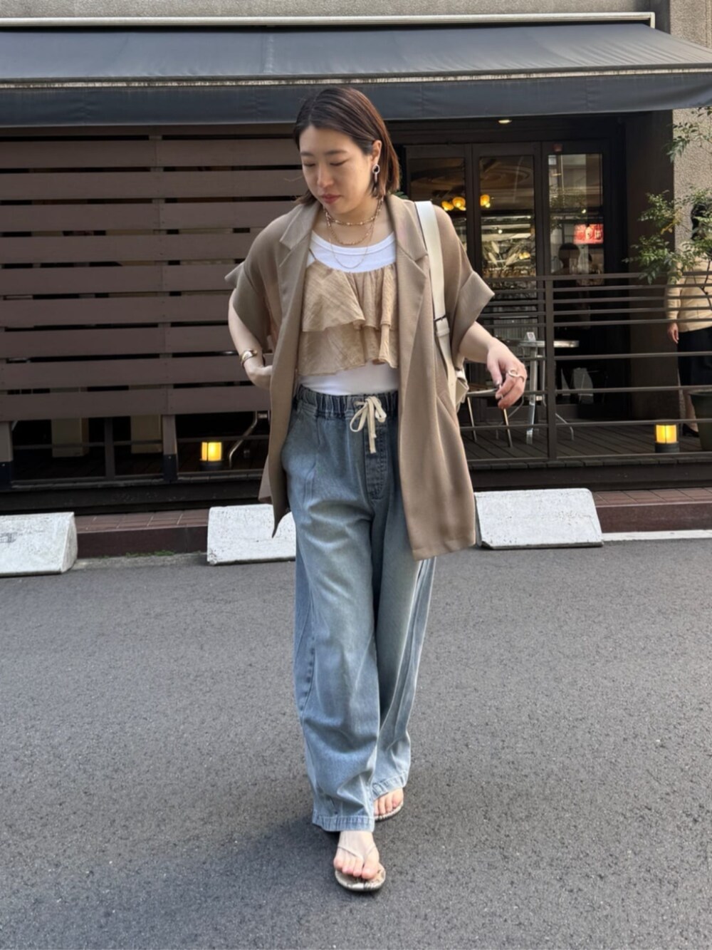 ホワイト系のショルダーバッグ、ブルー系のデニムパンツ、ブラウン系のテーラードジャケットを着用したレディースの春コーディネートの2枚目の写真