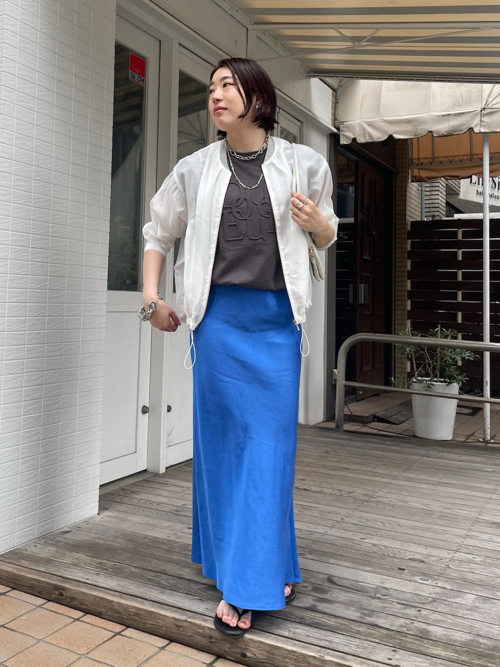 ブルー系のスカート、グレー系のTシャツ/カットソー、ホワイト系のブルゾンを着用したレディースの春コーディネートの2枚目の写真