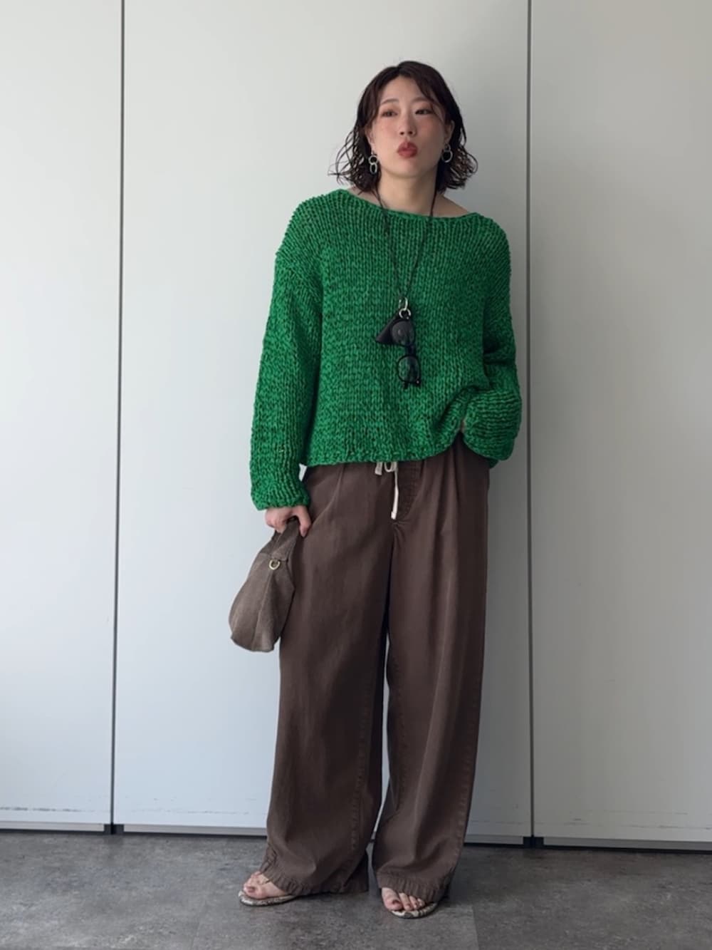 グリーン系のニット/セーター、ブラウン系のデニムパンツ、ブラウン系のネックレスを着用したレディースの秋コーディネートの5枚目の写真