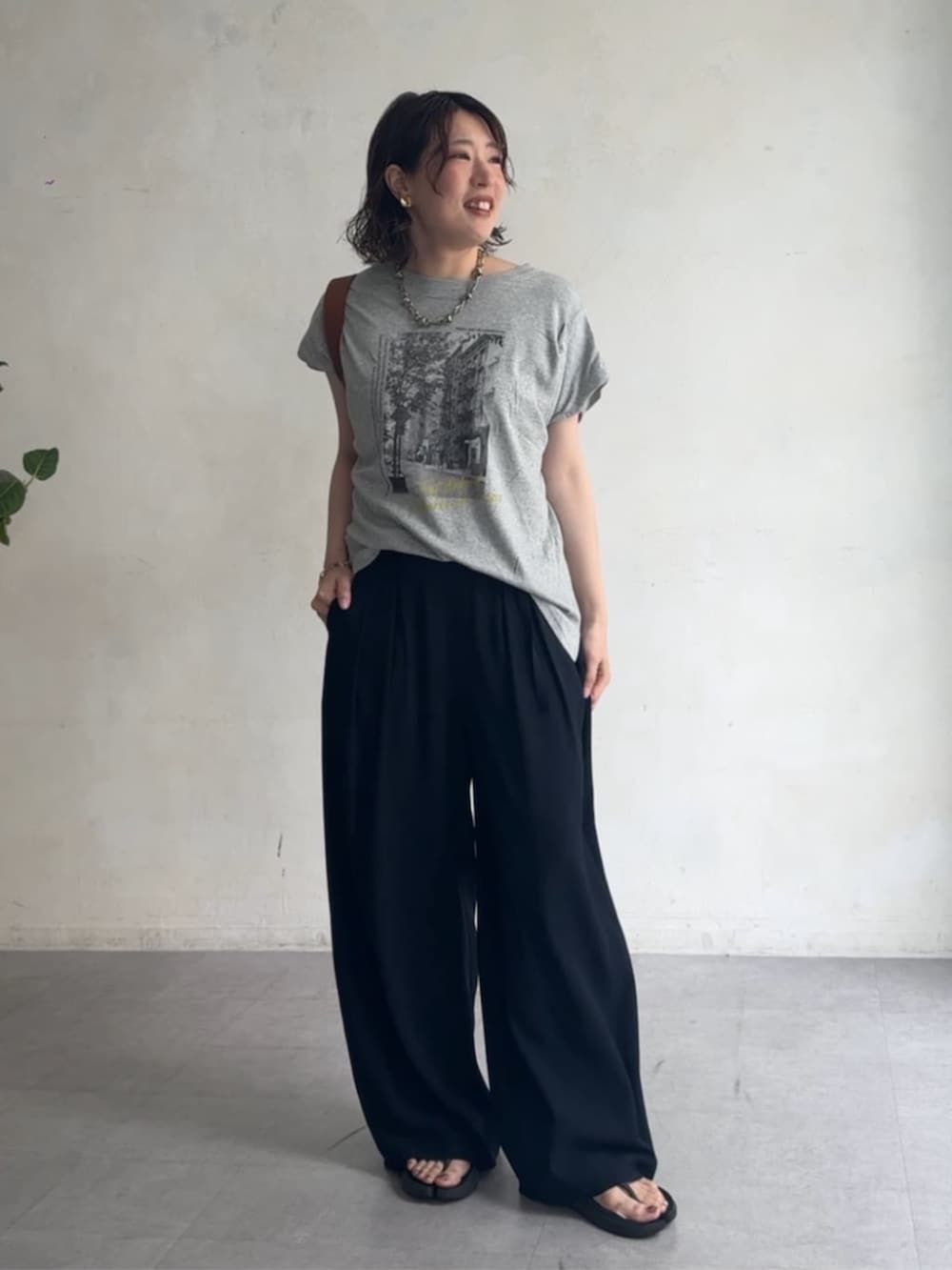ブルー系のスラックス、ブラウン系のサンダル、グレー系のTシャツ/カットソーを着用したレディースの夏コーディネートの2枚目の写真