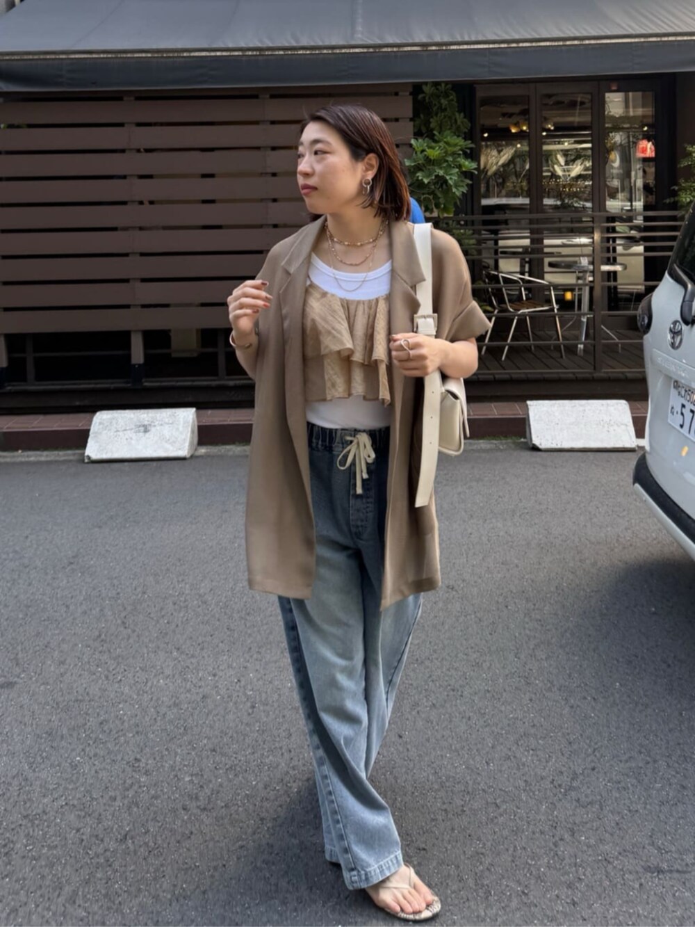 ホワイト系のショルダーバッグ、ブルー系のデニムパンツ、ブラウン系のテーラードジャケットを着用したレディースの春コーディネートの5枚目の写真