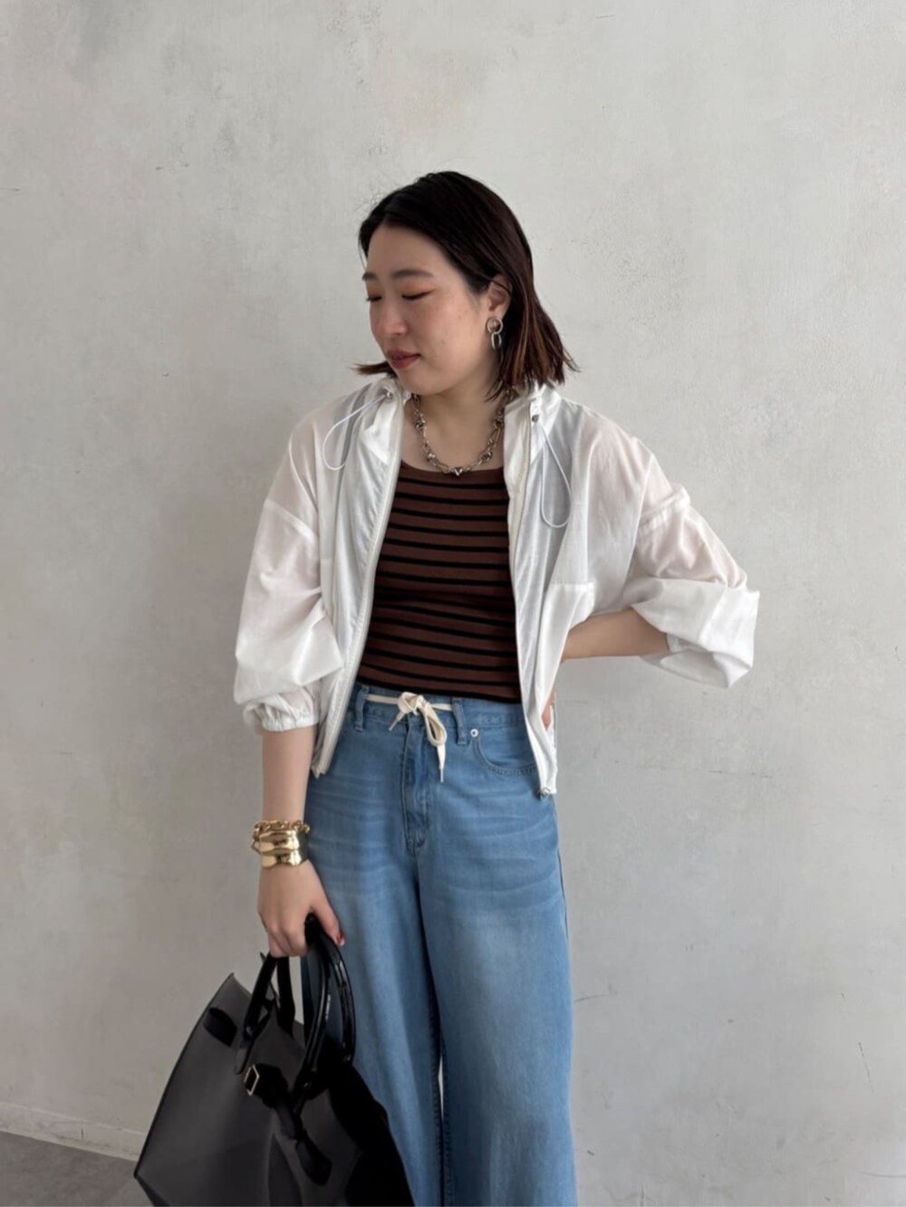 ブラック系のショルダーバッグ、ブルー系のデニムパンツ、ブラウン系のニット/セーターを着用したレディースの夏コーディネートの5枚目の写真