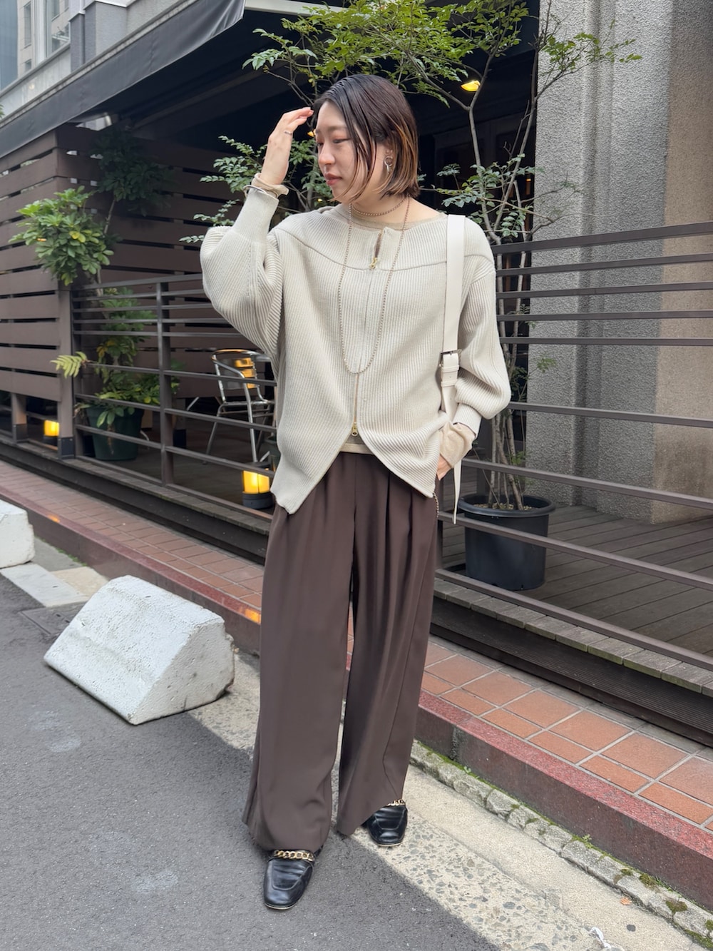 グレー系のニット/セーター、ブラウン系のスラックス、ゴールド系のTシャツ/カットソーを着用したレディースの冬コーディネートの2枚目の写真