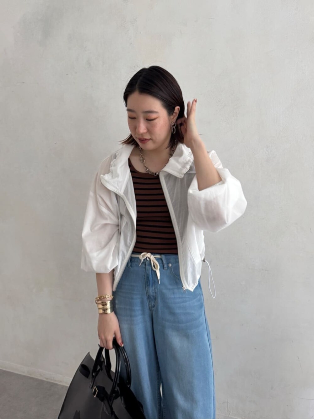 ブラック系のショルダーバッグ、ブルー系のデニムパンツ、ブラウン系のニット/セーターを着用したレディースの夏コーディネートの2枚目の写真