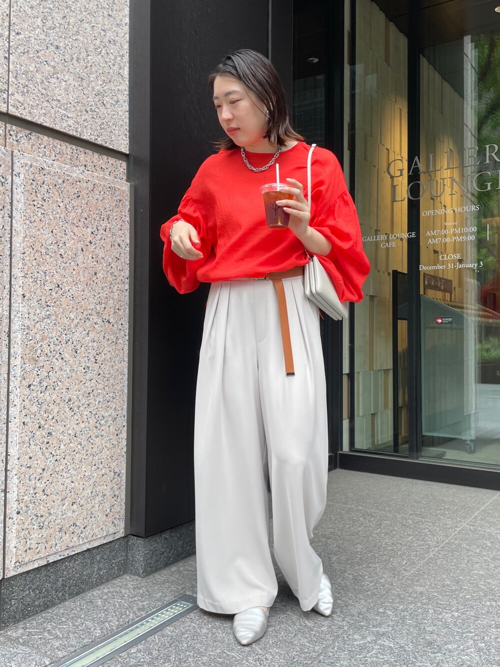 グレー系のスラックス、オレンジ系のシャツ/ブラウス、ホワイト系のショルダーバッグを着用したレディースの春コーディネートの2枚目の写真