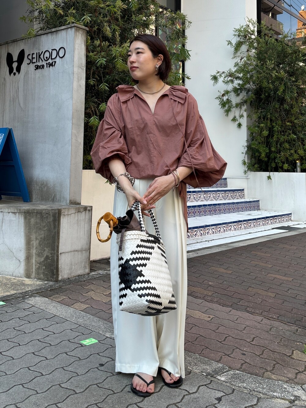 ホワイト系のスラックス、ブラウン系のシャツ/ブラウス、ホワイト系のかごバッグを着用したレディースの夏コーディネートの9枚目の写真