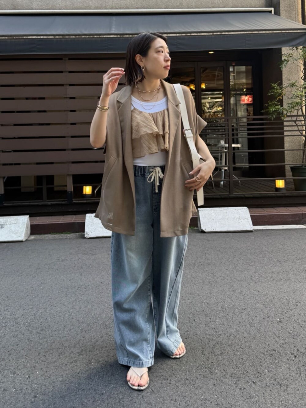 ホワイト系のショルダーバッグ、ブルー系のデニムパンツ、ブラウン系のテーラードジャケットを着用したレディースの春コーディネートの4枚目の写真