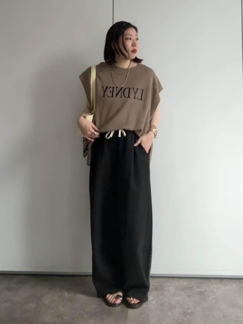 イエロー系のショルダーバッグ、ブラウン系のサンダル、ブラック系のデニムパンツを着用したレディースの夏コーディネートの4枚目の写真
