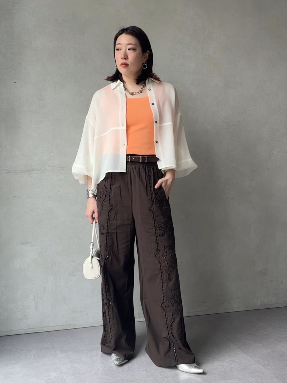 ブラウン系のその他パンツ、ホワイト系のシャツ/ブラウス、オレンジ系のニット/セーターを着用したレディースの春コーディネートの3枚目の写真