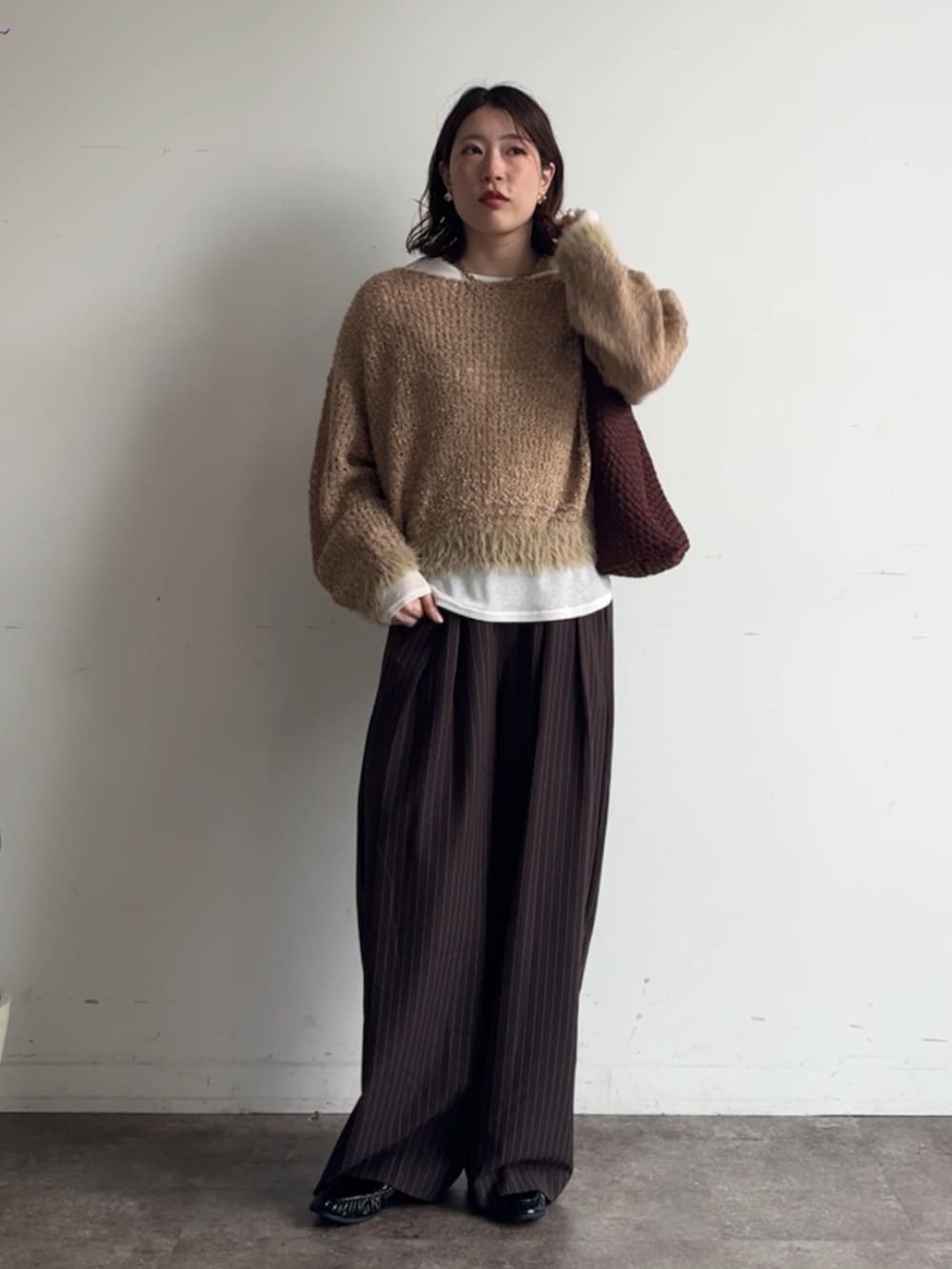 イエロー系のニット/セーター、ブラウン系のスラックス、ホワイト系のTシャツ/カットソーを着用したレディースの秋コーディネートの4枚目の写真