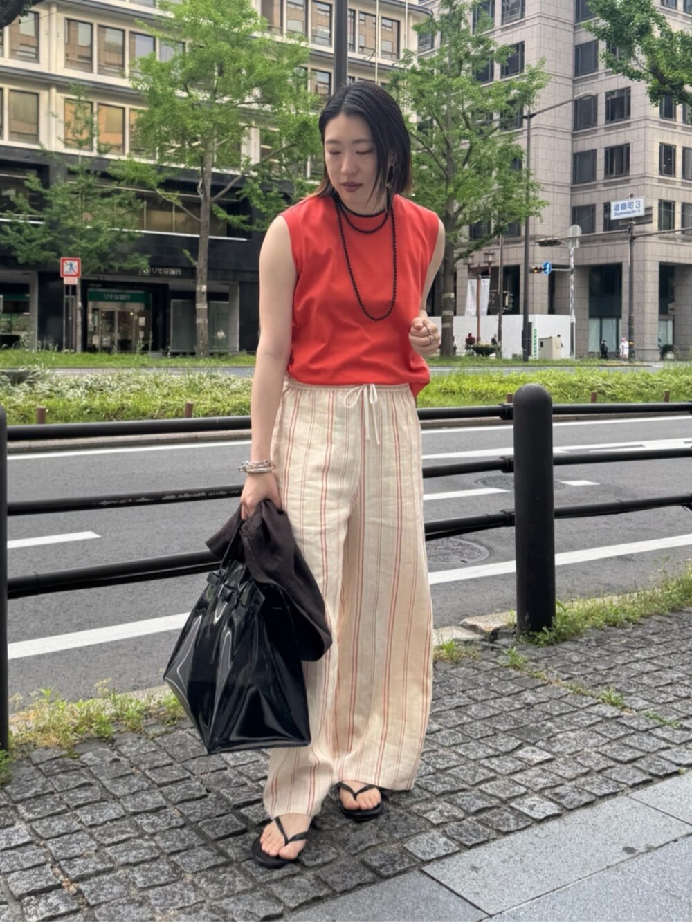 ブラック系のショルダーバッグ、オレンジ系のTシャツ/カットソー、ベージュ系のその他パンツを着用したレディースの夏コーディネートの2枚目の写真