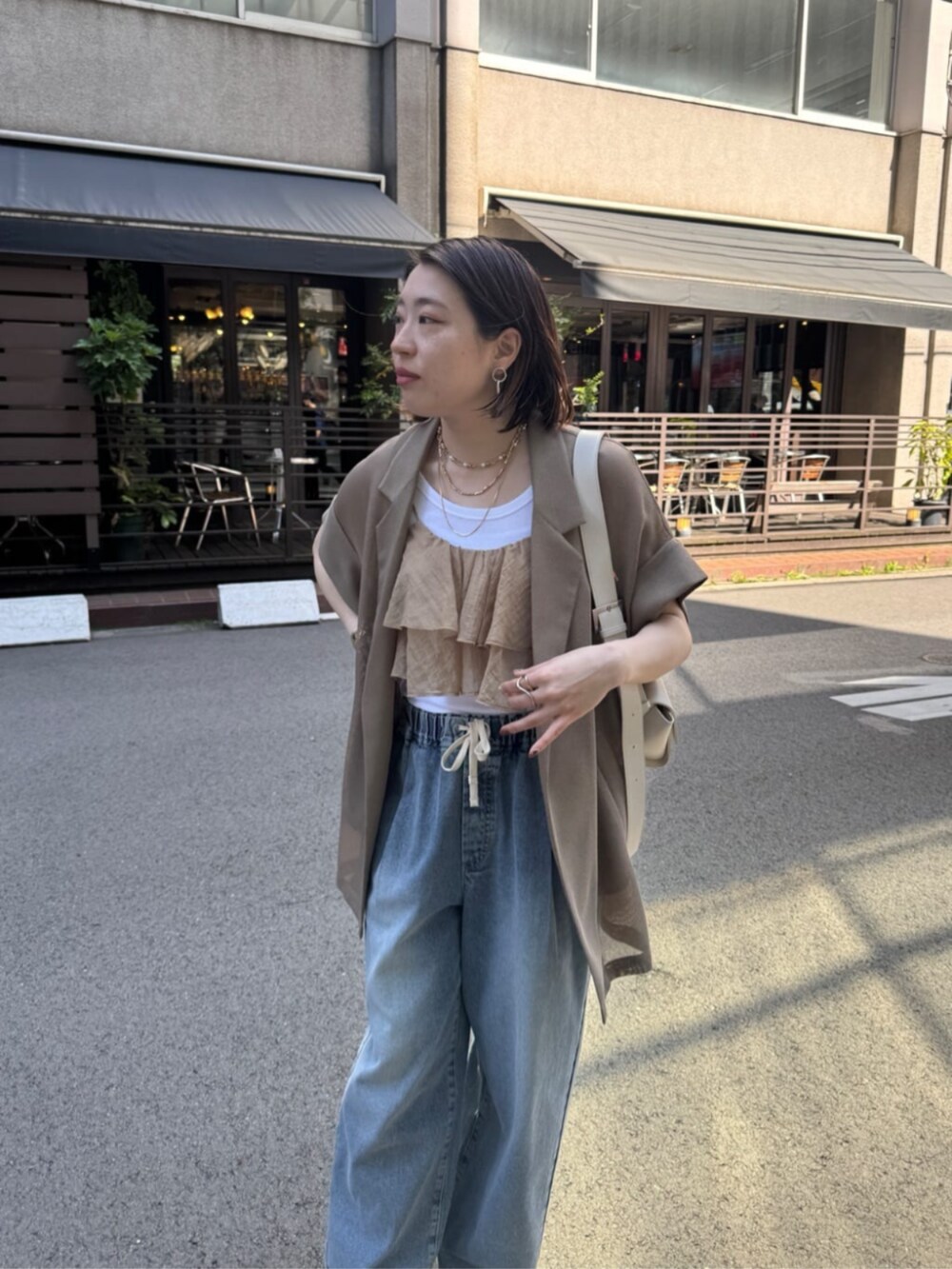 ホワイト系のショルダーバッグ、ブルー系のデニムパンツ、ブラウン系のテーラードジャケットを着用したレディースの春コーディネートの7枚目の写真