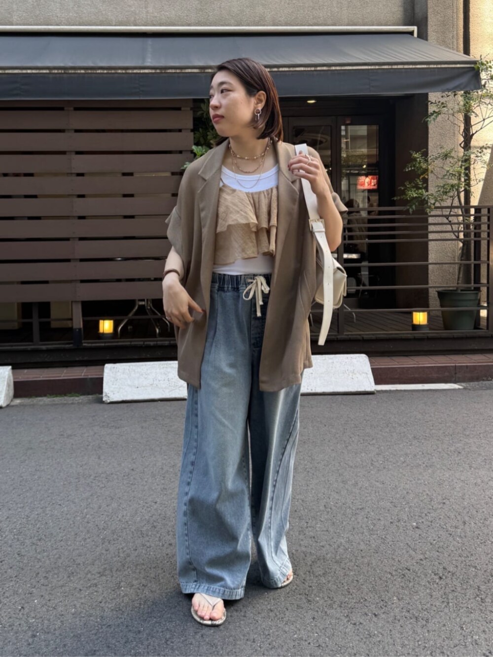 ホワイト系のショルダーバッグ、ブルー系のデニムパンツ、ブラウン系のテーラードジャケットを着用したレディースの春コーディネートの3枚目の写真