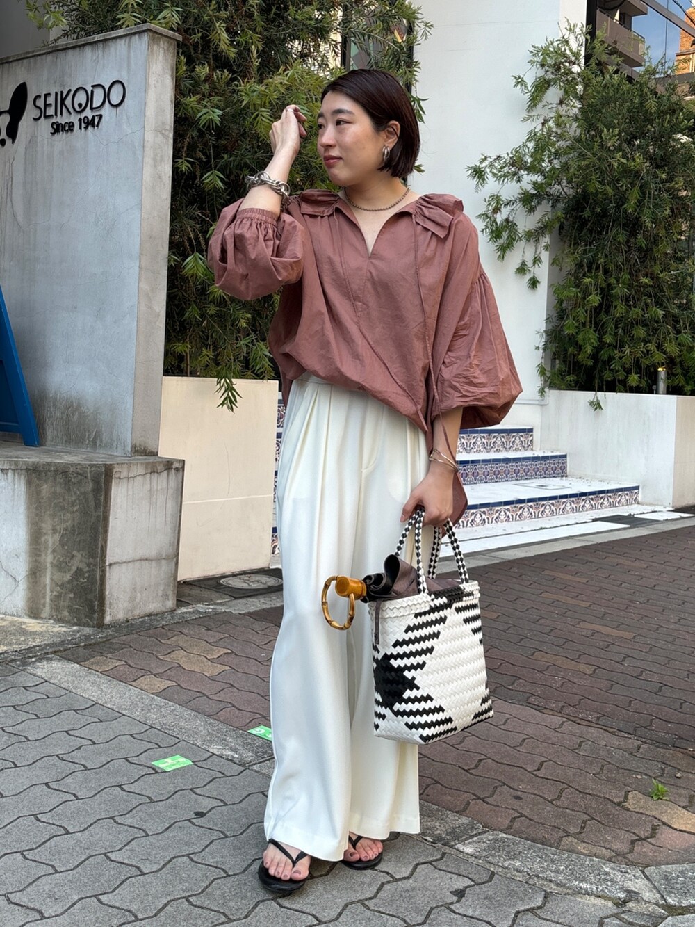 ホワイト系のスラックス、ブラウン系のシャツ/ブラウス、ホワイト系のかごバッグを着用したレディースの夏コーディネートの3枚目の写真