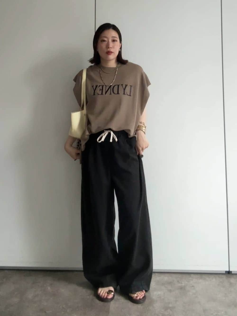 イエロー系のショルダーバッグ、ブラウン系のサンダル、ブラック系のデニムパンツを着用したレディースの夏コーディネートの3枚目の写真