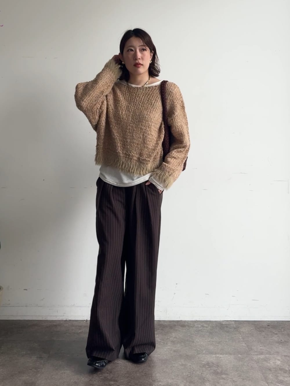 イエロー系のニット/セーター、ブラウン系のスラックス、ホワイト系のTシャツ/カットソーを着用したレディースの秋コーディネートの2枚目の写真
