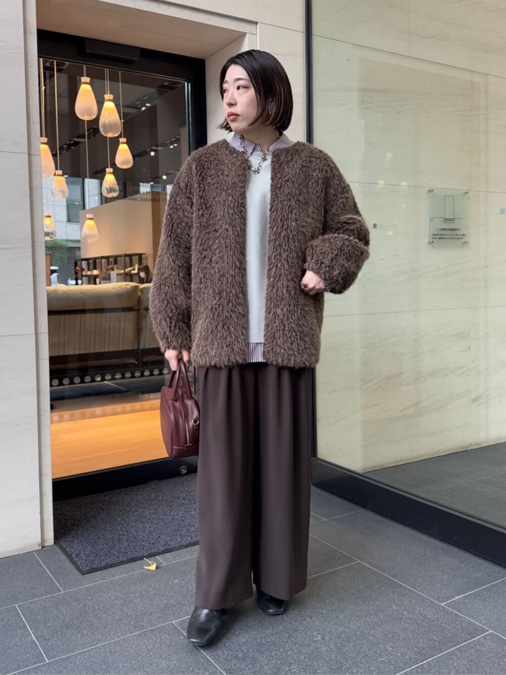 ブラウン系のスラックス、レッド系のシャツ/ブラウス、ブラウン系のショルダーバッグを着用したレディースの冬コーディネートの2枚目の写真