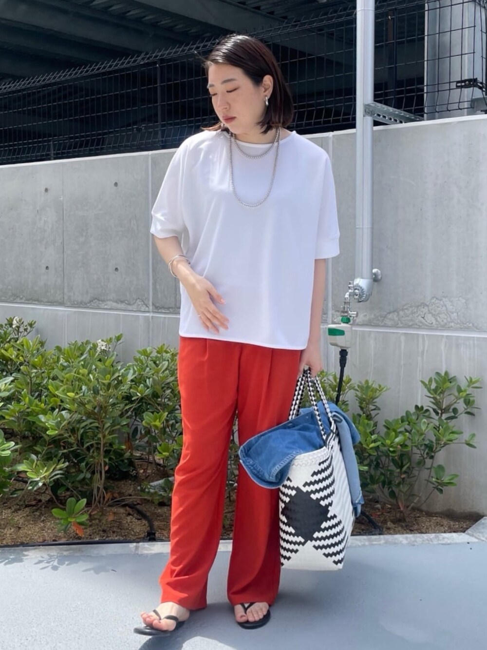 ホワイト系のシャツ/ブラウス、オレンジ系のスラックス、ホワイト系のかごバッグを着用したレディースの夏コーディネートの2枚目の写真