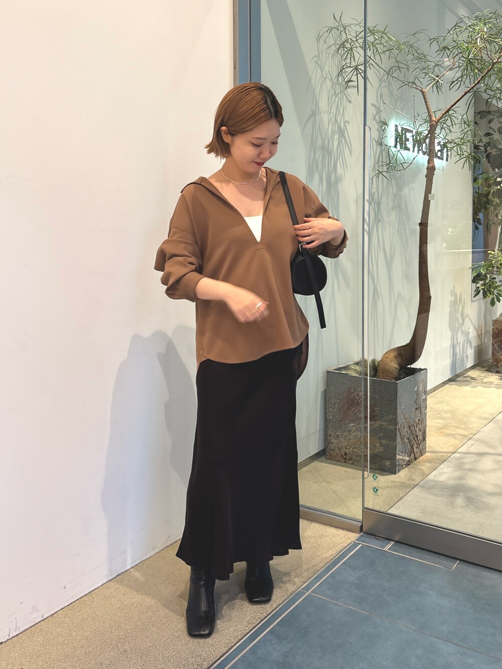 ブラウン系のスカート、ブラック系のショルダーバッグ、ホワイト系のキャミソールを着用したレディースの秋コーディネートの2枚目の写真
