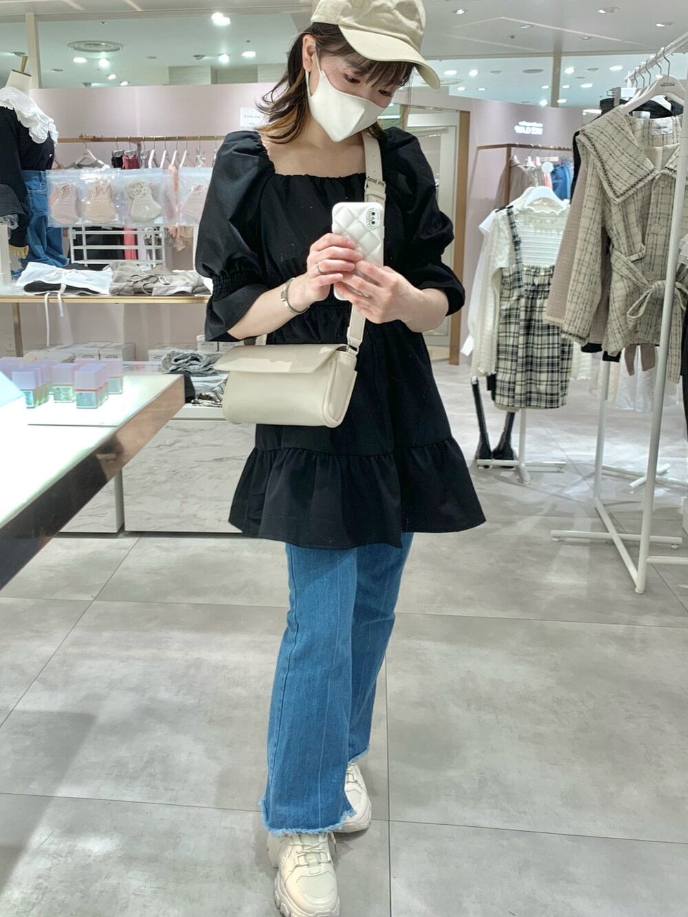 ブラック系のチュニック、ホワイト系のボディバッグ/ウエストポーチ、ブルー系のデニムパンツを着用したレディースの春コーディネートの2枚目の写真