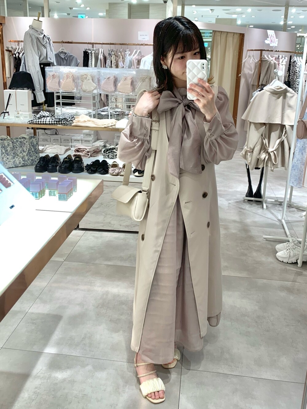 ベージュ系のトレンチコート、ホワイト系のサンダル、ホワイト系のボディバッグ/ウエストポーチを着用したレディースの春コーディネートの2枚目の写真