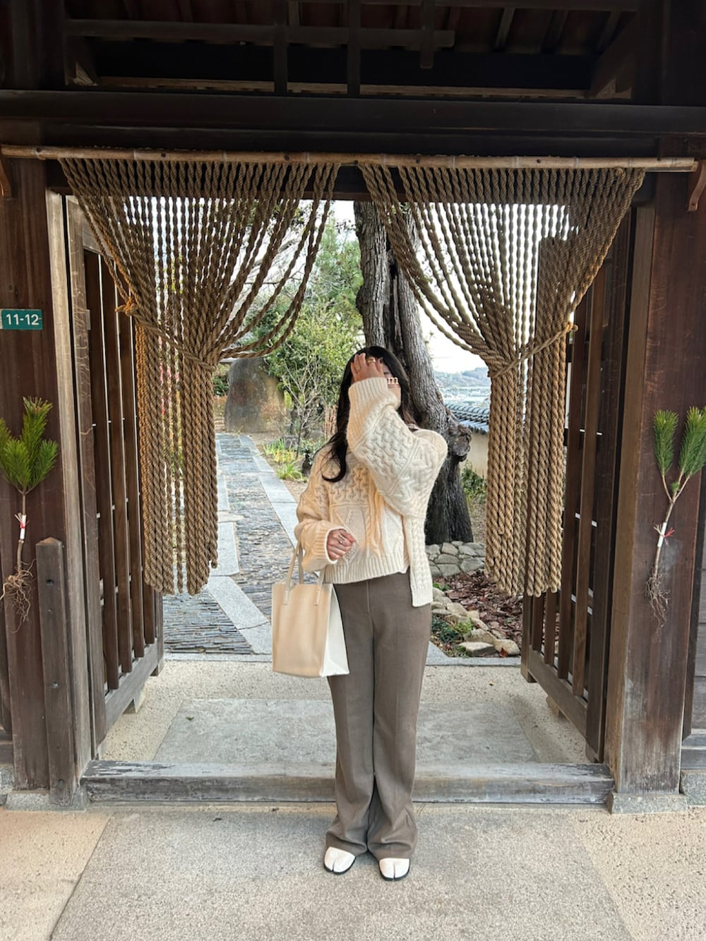 ブラウン系のパンツ、ホワイト系のブーツ、ベージュ系のハンドバッグを着用したレディースの冬コーディネートの2枚目の写真