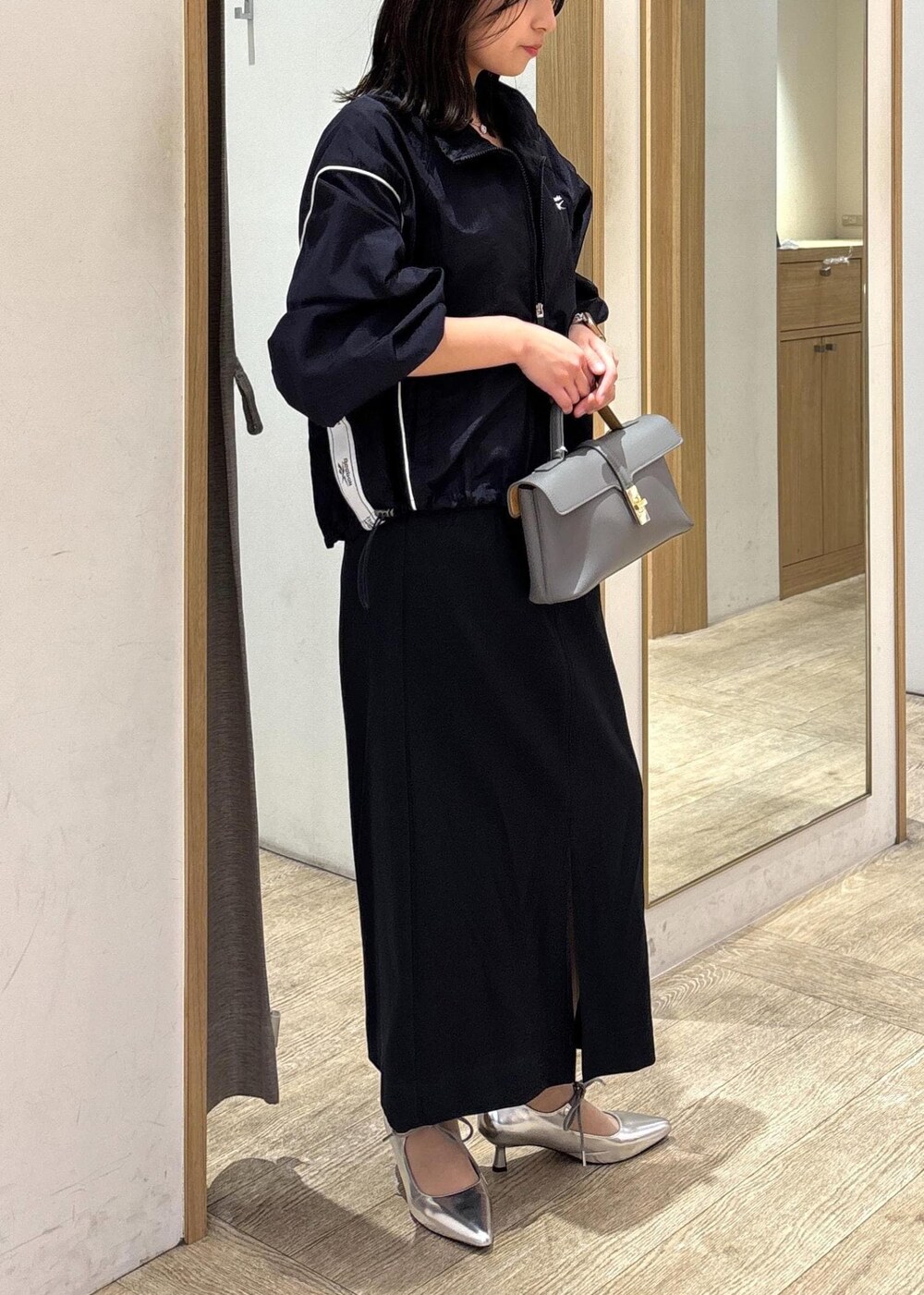 グレー系のショルダーバッグ、ブルー系のスカート、シルバー系のパンプスを着用したレディースの春コーディネートの2枚目の写真
