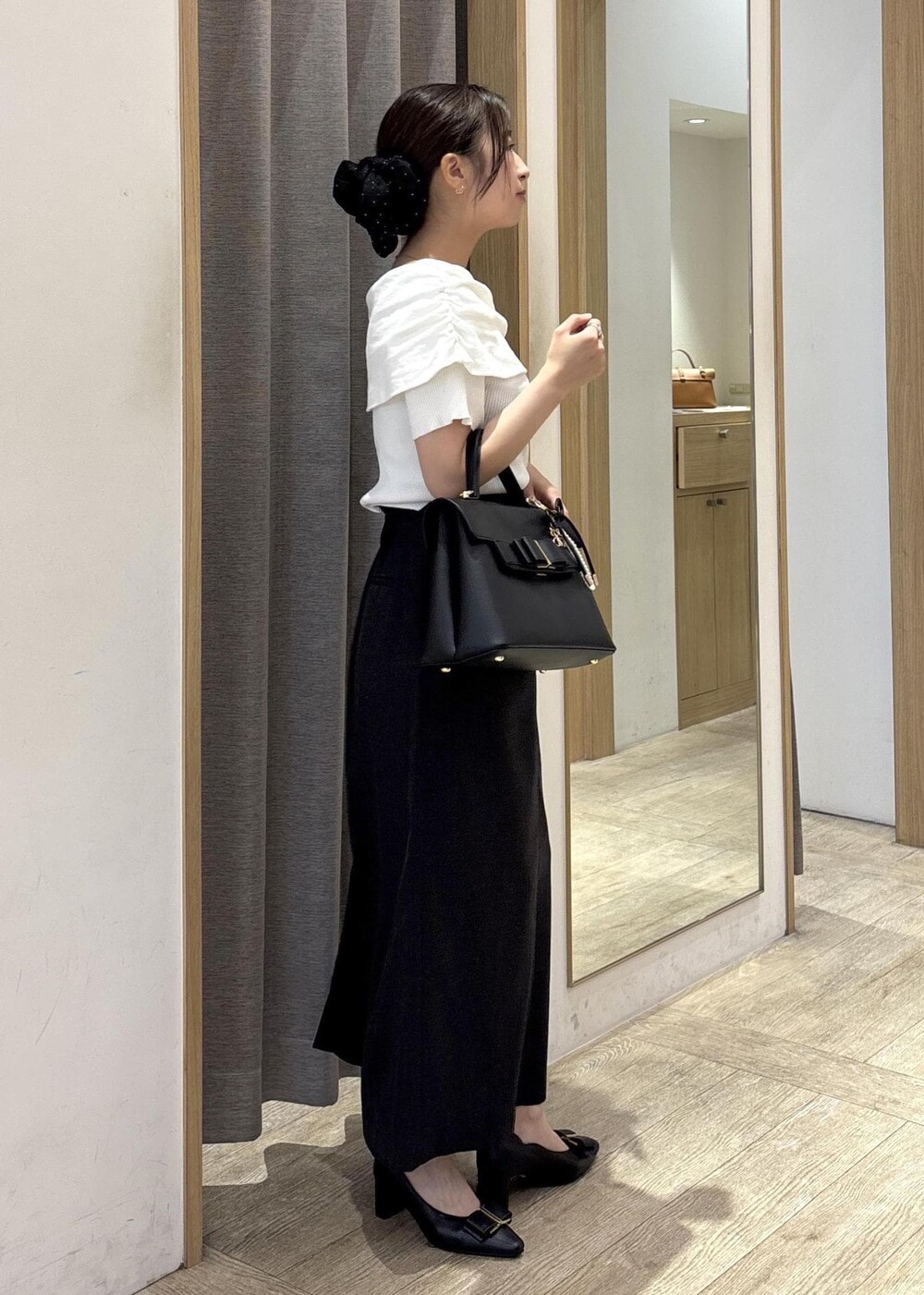 ブラック系のパンプス、ブラック系のハンドバッグ、ホワイト系のニット/セーターを着用したレディースの春コーディネートの2枚目の写真