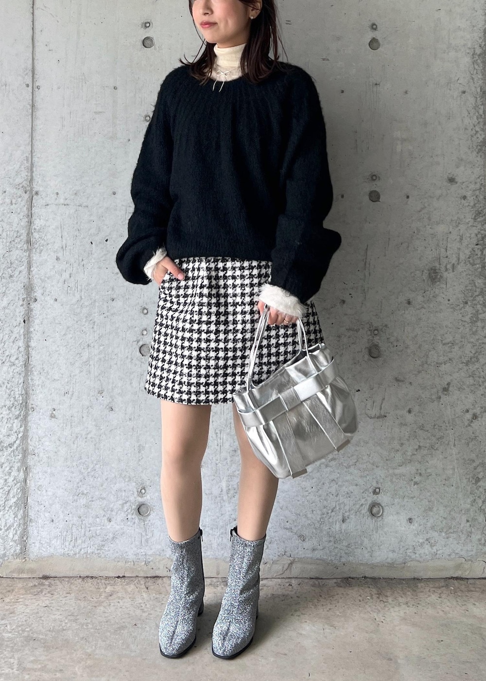 シルバー系のブーツ、ブラック系のスカート、ホワイト系のニット/セーターを着用したレディースの冬コーディネートの2枚目の写真