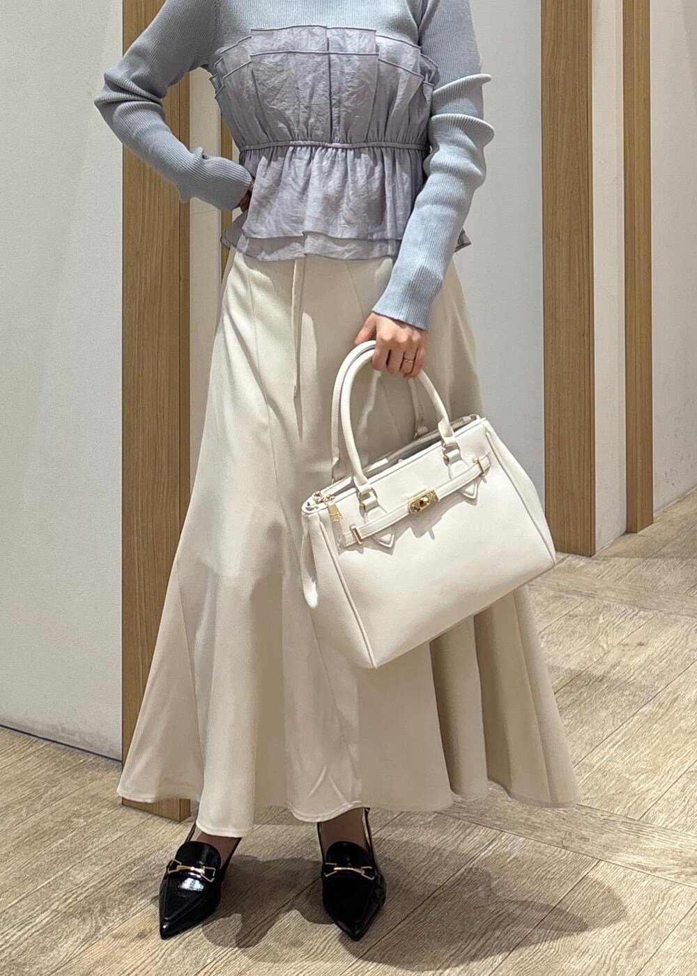 ブラック系のパンプス、ベージュ系のスカート、ブルー系のニット/セーターを着用したレディースの春コーディネートの2枚目の写真