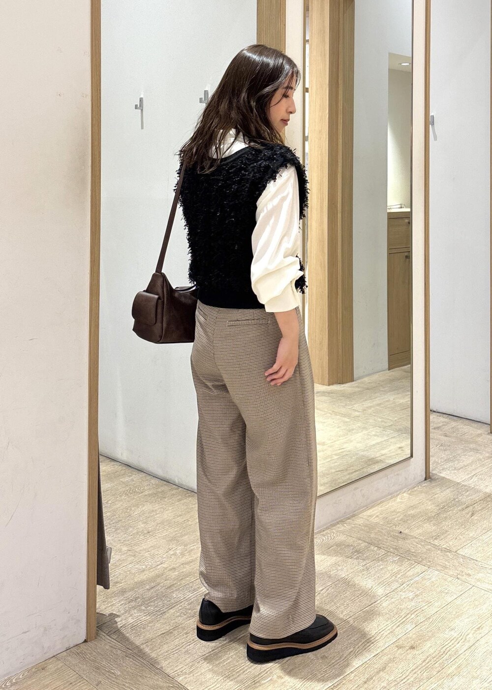 ベージュ系のスラックス、ブラウン系のショルダーバッグ、ブラック系のベストを着用したレディースの秋コーディネートの5枚目の写真