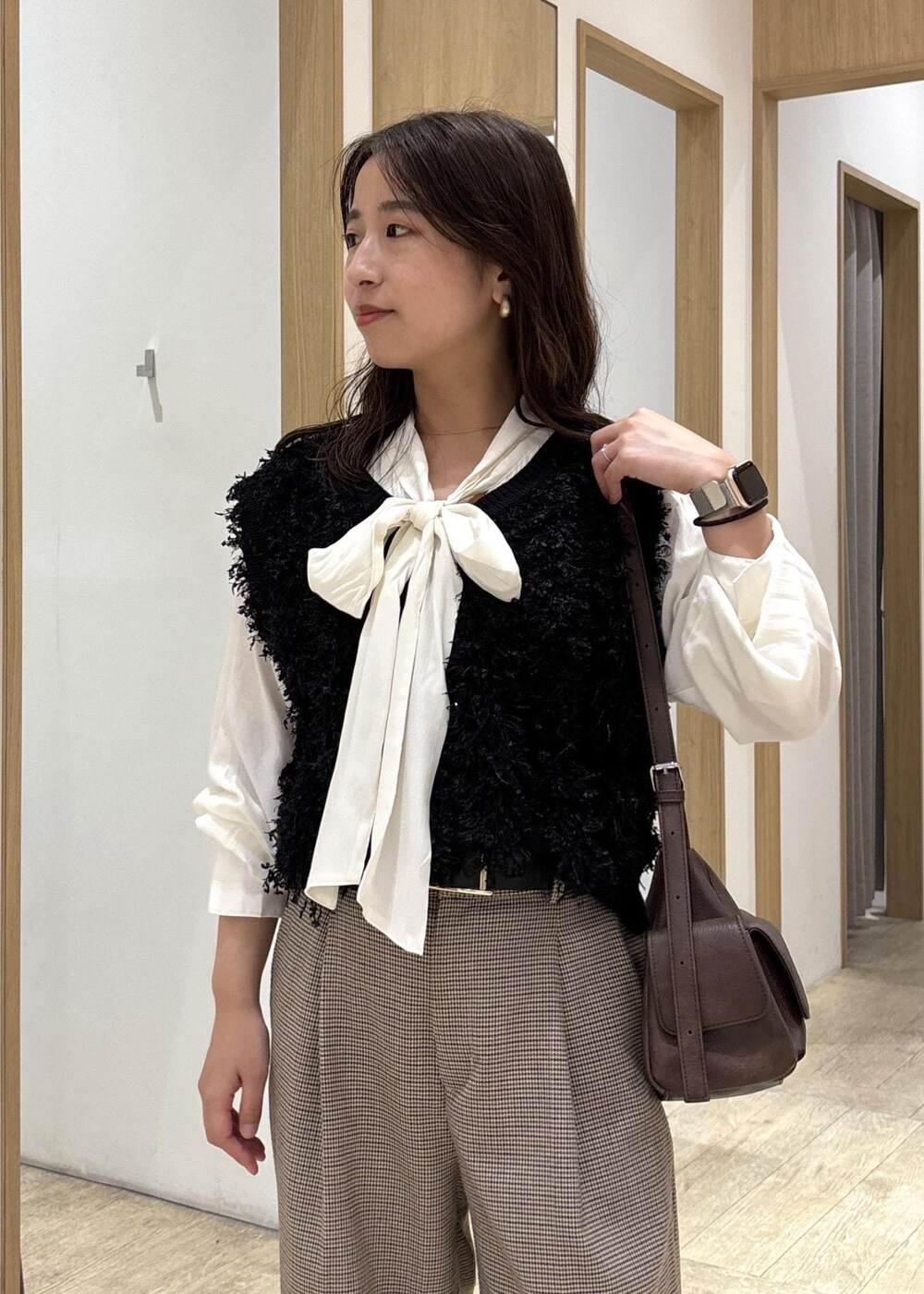 ベージュ系のスラックス、ブラウン系のショルダーバッグ、ブラック系のベストを着用したレディースの秋コーディネートの6枚目の写真