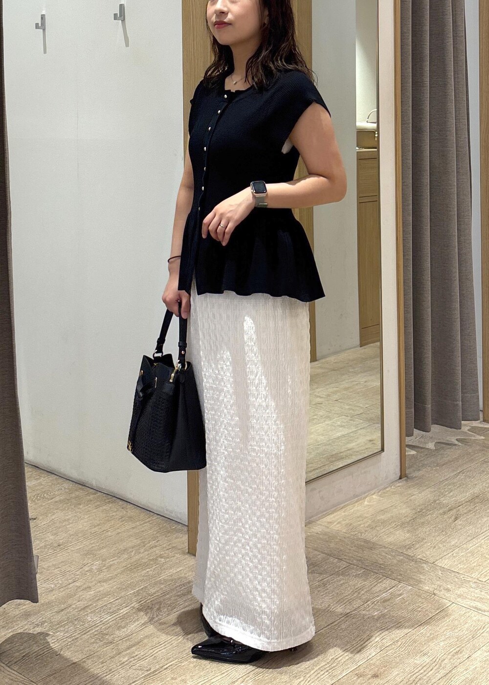 ブラック系のパンプス、ホワイト系のスカート、ブラック系のショルダーバッグを着用したレディースの夏コーディネートの2枚目の写真